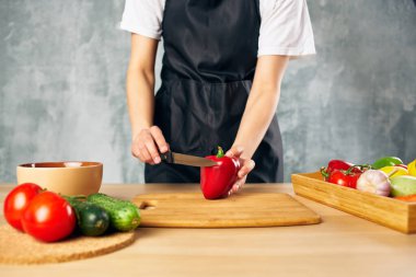 Mutfakta siyah önlüklü bir kadın sebze kesiyor.