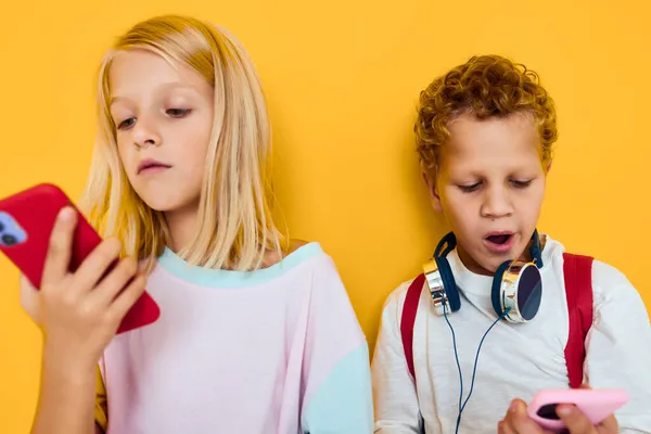 Foto di due bambini piccoli ragazza guardando in uno smartphone e giocando giochi sfondo giallo — Foto Stock