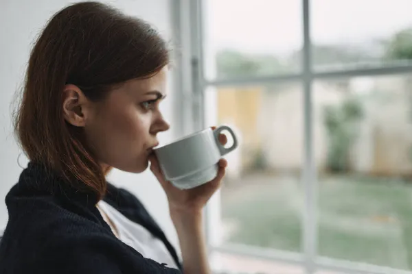 Женщина с чашкой чая в руке возле окна портрет вид сбоку — стоковое фото