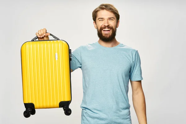 Szakállas férfi bőrönddel a kezében és kék pólóban, világos háttérrel — Stock Fotó