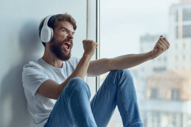 Sakallı adam pencere eşiğinde oturuyor.