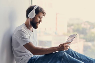 Neşeli adam pencere kenarındaki teknolojide oturuyor.