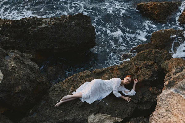 Beautiful bride in long white dress wet hair lying on a rocky cliff unaltered — Stock Photo, Image