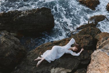 Güzel gelin, kayalık bir deniz kıyısında sırt üstü uzanıyor. Yaz tatili konsepti.