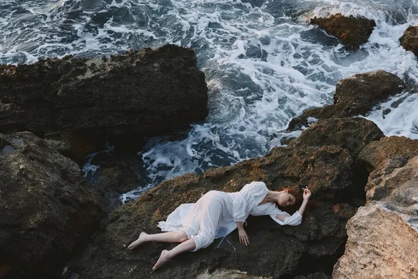 Barfota kvinna i en avskild plats på en vild stenig kust i en vit klänning vy ovanifrån — Stockfoto
