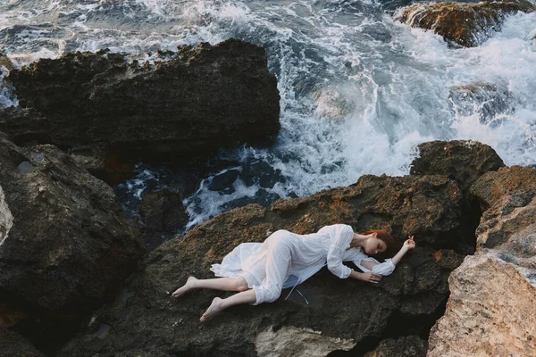 赤脚女人躺在岩石海岸上，岩石表面的裂缝没有改变 — 图库照片