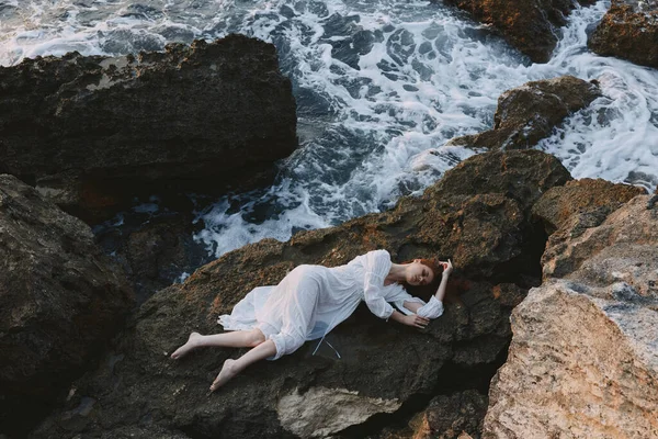 在荒芜的岩石海岸上的一个僻静的地方，站在一个赤脚的女人面前，从上方眺望着白色的连衣裙 — 图库照片