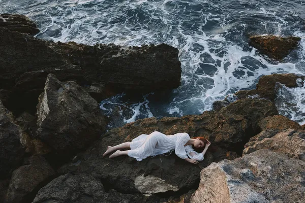 穿着白色长裙、头发湿湿的女人躺在岩石悬崖上的自然景观 — 图库照片