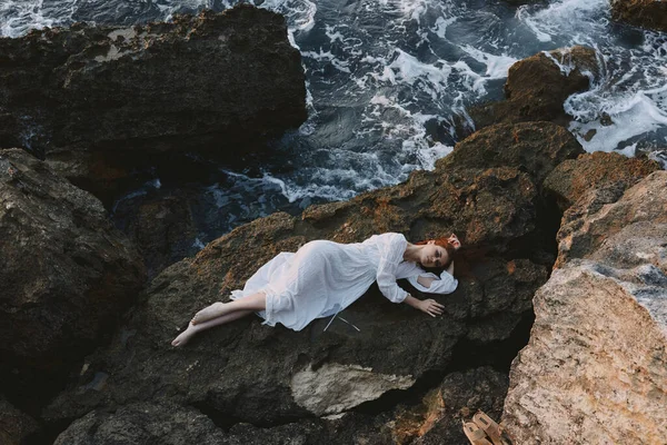 一个性感的女人躺在岩石海岸上，岩石表面有裂缝 — 图库照片