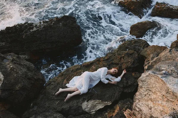 美丽的新娘，身穿白色长裙，头发湿透，躺在岩石峭壁上 — 图库照片