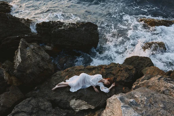 Woman in long white dress wet hair lying on a rocky cliff nature landscape — Stock Photo, Image