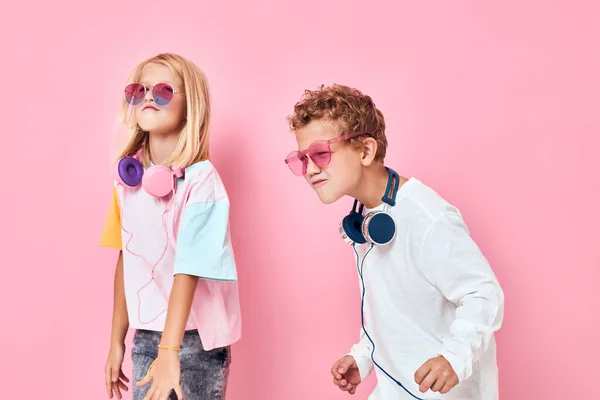 Retrato de una chica y un niño en gafas de sol divertirse con los amigos de color rosa de fondo — Foto de Stock