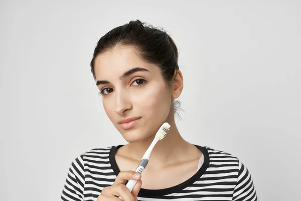Mulher em uma escova de dentes de t-shirt listrada na mão luz de fundo — Fotografia de Stock