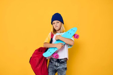 Başında kaykayı olan, sarı arka planda sevimli, sarışın bir kız.