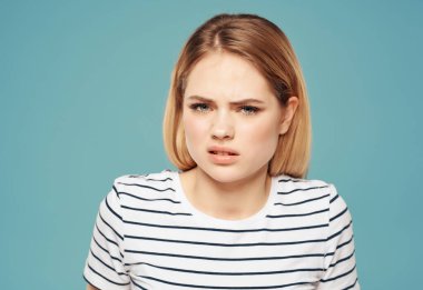 Yüzünde çizgili tişört teneke tabağı ve elleri mavi arka planı olan kızgın bir kadın.