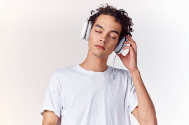Beyaz tişörtlü, kulaklıklı, müzik teknolojisi olan kıvırcık saçlı adam.