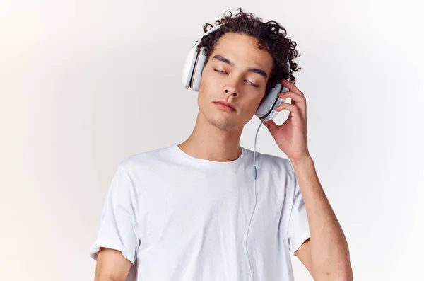 Kudrnatý chlap v bílém tričku se sluchátky hudba technologie zábava — Stock fotografie