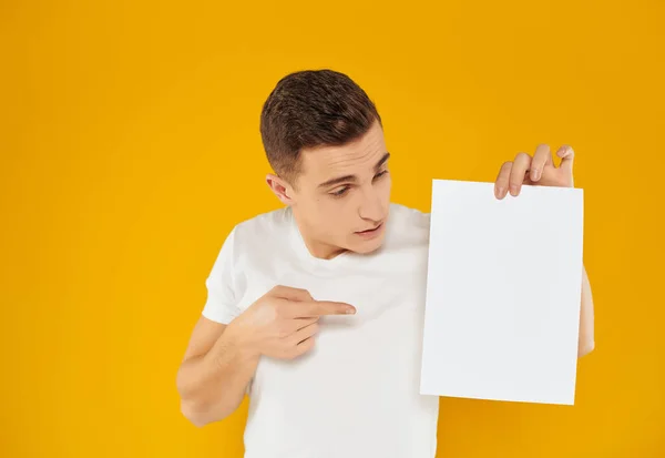 Man in wit t-shirt blad van papier reclame presentatie gele achtergrond — Stockfoto