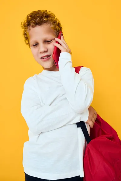 Engraçado adolescente falando ao telefone com uma mochila escolar fundo amarelo — Fotografia de Stock