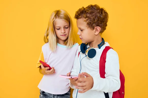 Lindos niños mirando en un teléfono inteligente y jugando juegos de fondo amarillo —  Fotos de Stock