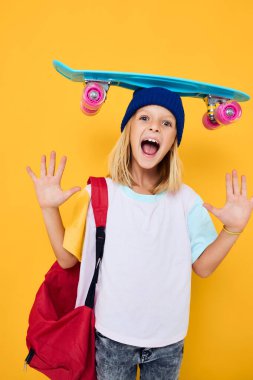 Beyaz tişörtlü okul kızı elinde kaykayla poz veriyor.