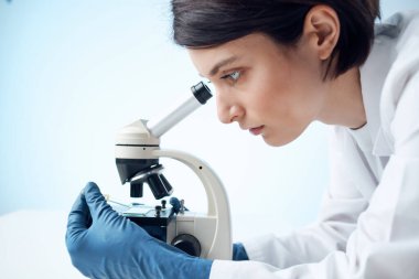 Laboratuvar asistanı, mikroskop araştırma biyoteknolojisi yakın planında oturuyor.