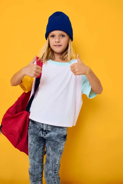 Schoolgirl gestures with her hands in blue hats on a yellow background — Stock Photo, Image
