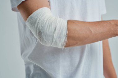 Elinde bandajlı hastane ilacı olan beyaz tişörtlü hasta bir adam.