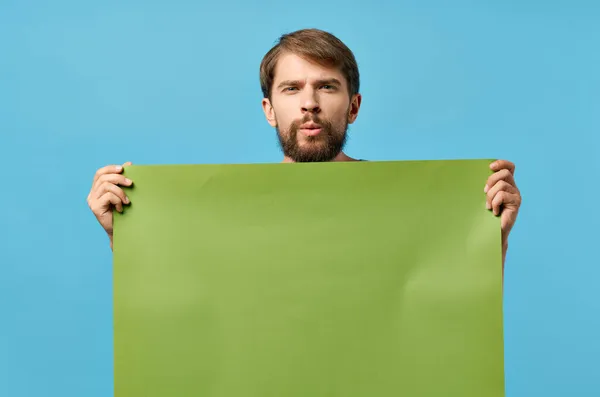 녹색 흉내 내기 포스터를 들고 있는 잘생긴 남자푸른 배경 평가 — 스톡 사진