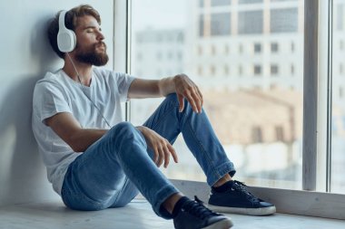 Kulaklıkla pencere eşiğinde oturan adam moda.