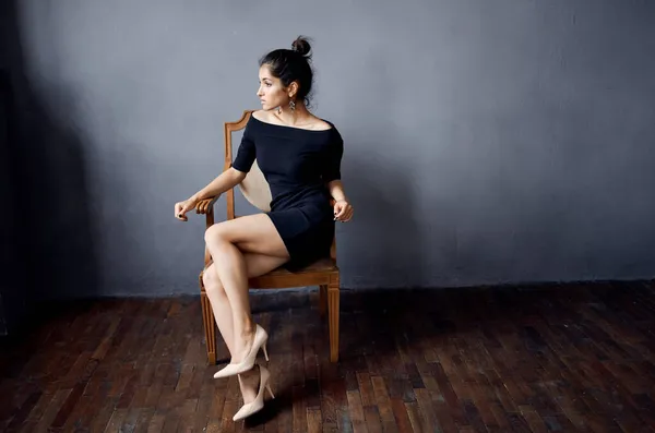 Μελαχρινή σε μαύρο φόρεμα κοντά στην καρέκλα πολυτελές στούντιο lifestyle μόδας — Φωτογραφία Αρχείου