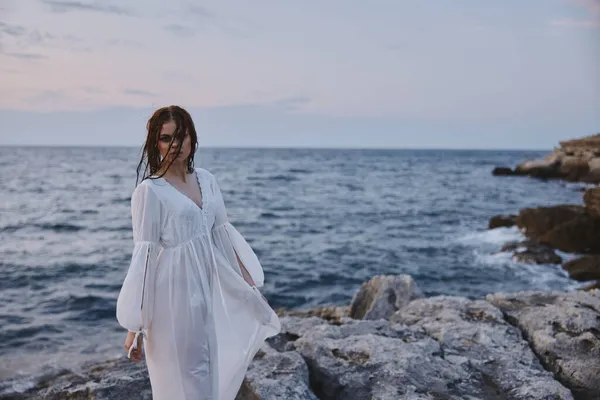 Une femme en robe blanche se tient sur les pierres sur le rivage de l'océan Voyage — Photo