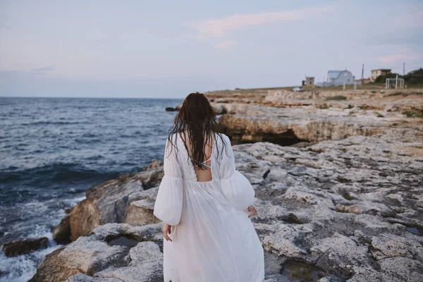Beyaz elbiseli bir kadın kayalıklarda yürür. — Stok fotoğraf