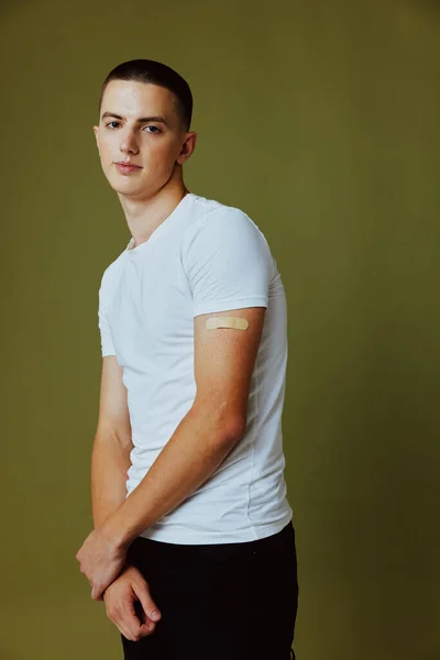 Jóképű férfi fehér pólóban, ragtapasszal a karján védettség elleni védőoltás útlevéllel. — Stock Fotó