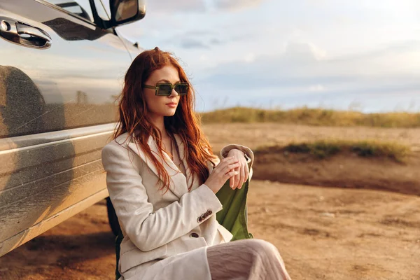 Piękna kobieta siedzi na krześle na polu w ciemnych okularach w pobliżu samochodu niekończące się pole — Zdjęcie stockowe