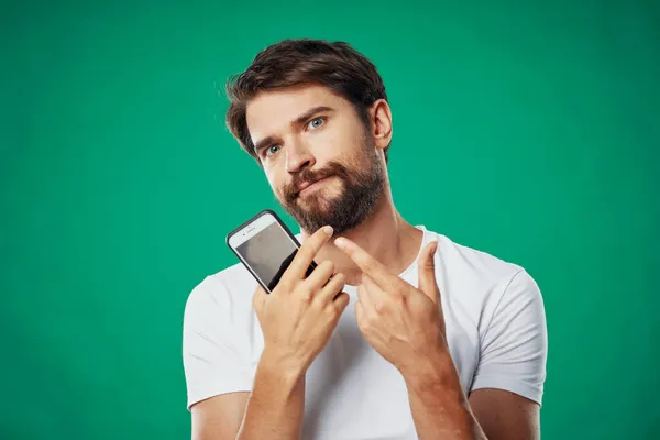 Hombre en una camiseta con un teléfono en la mano sobre un fondo verde vista recortada — Foto de Stock