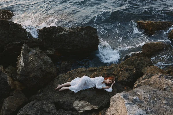 Hermosa mujer en vestido blanco largo cabello mojado acostado en un acantilado rocoso concepto de vacaciones — Foto de Stock