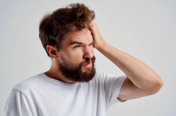 Man met baard in een wit t-shirt hoofdpijn migraine problemen lichte achtergrond — Stockfoto
