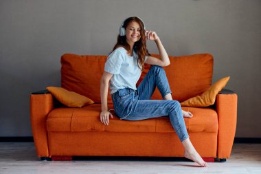 Portakal rengi kanepe teknolojisinde kulaklıkla müzik dinleyen bir kadının portresi