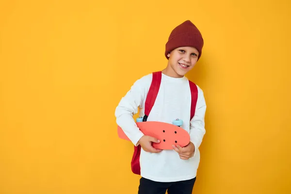 白いセーターのかわいい男の子の肖像スケートボードエンターテイメント黄色の背景 — ストック写真