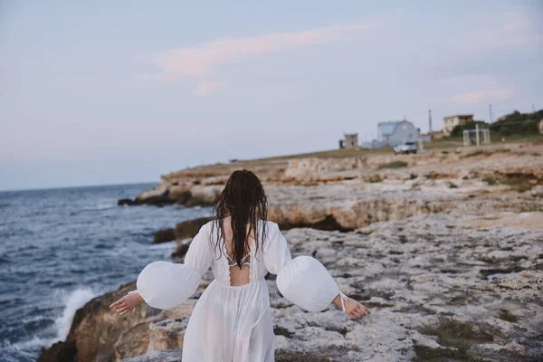 Beyaz elbiseli kadın plaj taşlarında yürüyor. — Stok fotoğraf