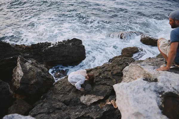 Женщина в белом платье сидит на камнях у океана — стоковое фото