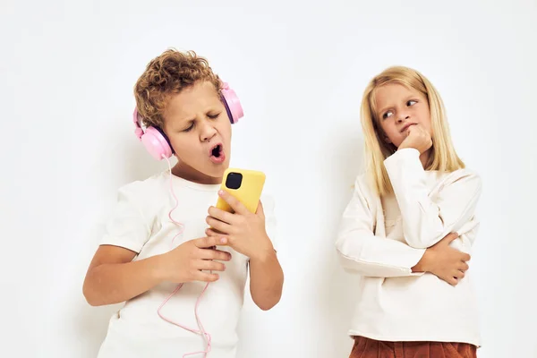 Dvě předškolní děti chlapec a dívka sluchátka s telefonem zábava světlo pozadí — Stock fotografie