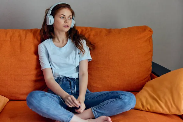 Jolie femme sur le canapé orange écoutant de la musique avec écouteurs Lifestyle — Photo
