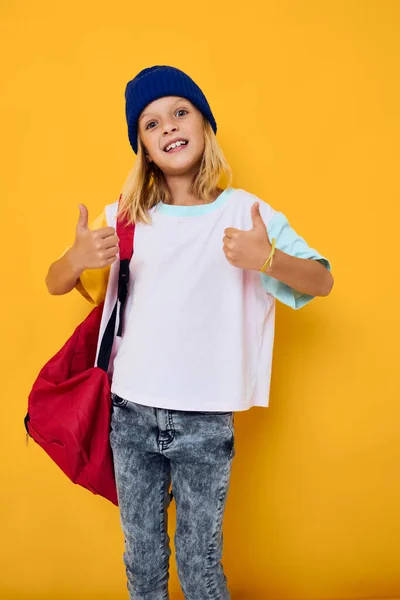 Bonito menina mostrando polegares até escola amarelo fundo — Fotografia de Stock