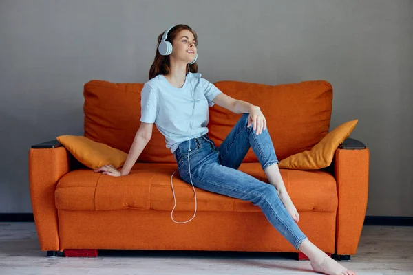 Beautiful woman sitting on the couch at home listening to music on headphones Lifestyle — Stock Photo, Image