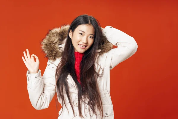 Frau asiatischen Aussehens in Winterjacke modische Kleidung roter Hintergrund — Stockfoto