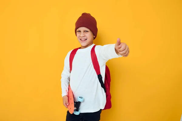 Glada liten unge i en röd hatt skateboard i händerna isolerad bakgrund — Stockfoto