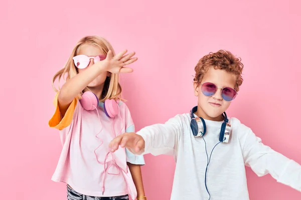 Srandovní malý chlapec a dívka v slunečních brýlích bavit s přáteli růžové barvy pozadí — Stock fotografie