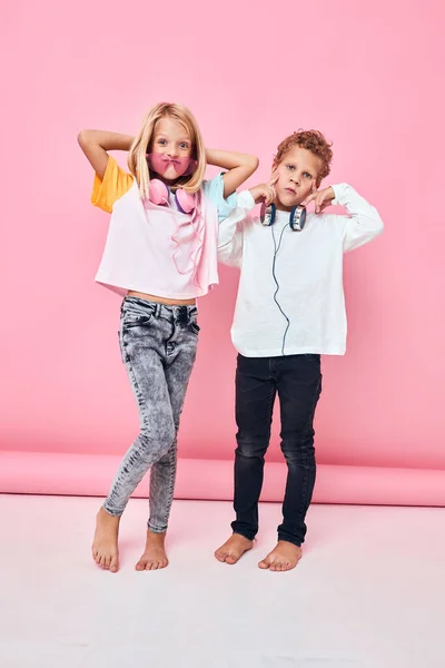 Niño y niña de pie lado a lado usando auriculares posando fondo rosa —  Fotos de Stock